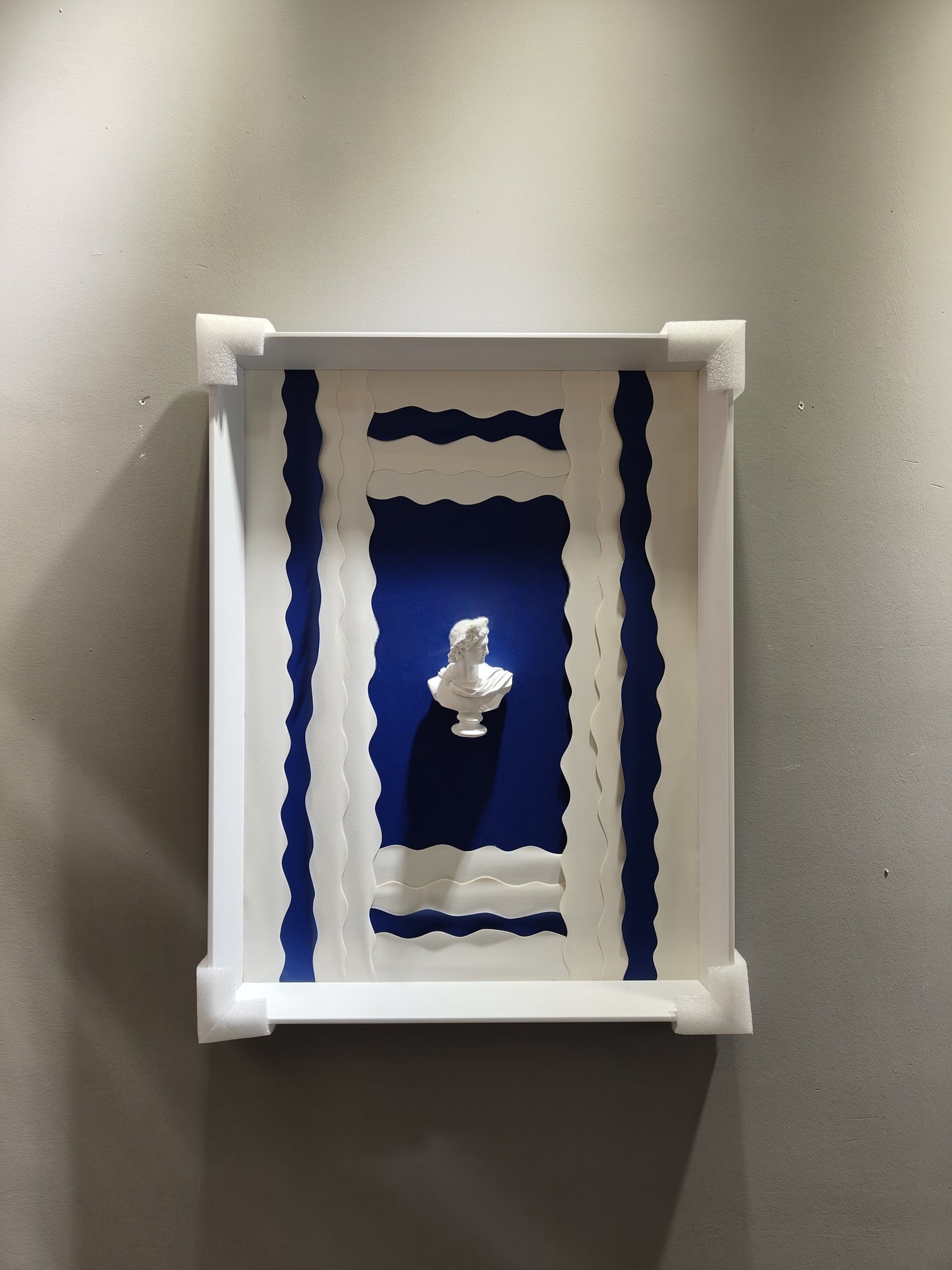 Modern wave sculpture wall art featuring a classical white bust on a layered blue and white background with a white frame