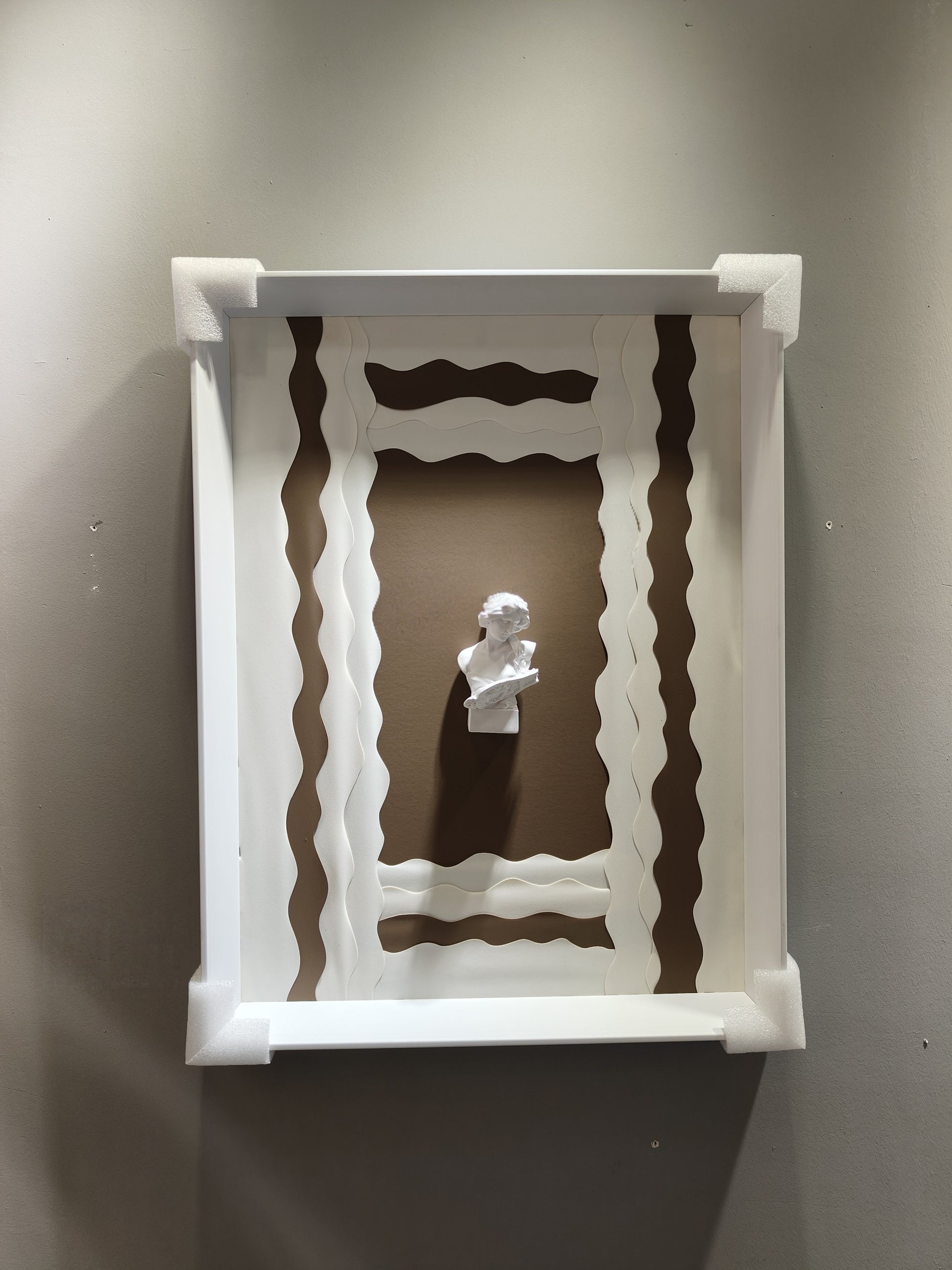 Minimalist wall art with wavy white frame and 3D plaster bust on taupe background

